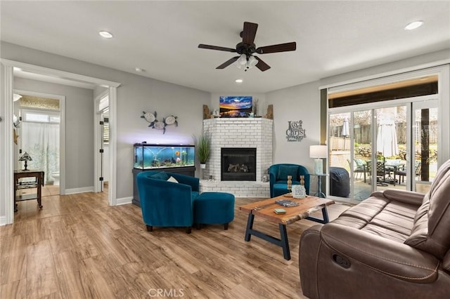 living area with light wood finished floors, a brick fireplace, baseboards, and recessed lighting