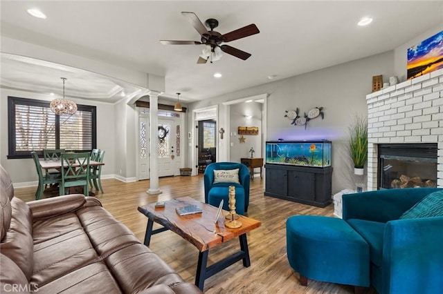 living room featuring a brick fireplace, recessed lighting, wood finished floors, and ornate columns