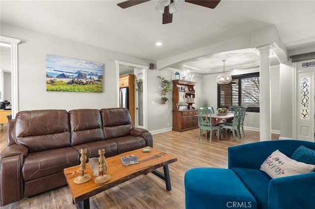 living area with baseboards, light wood finished floors, ceiling fan with notable chandelier, and ornate columns