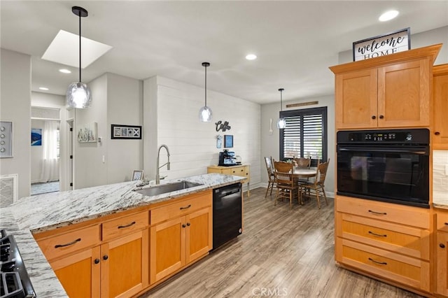 kitchen with light wood-style floors, light stone counters, black appliances, pendant lighting, and a sink