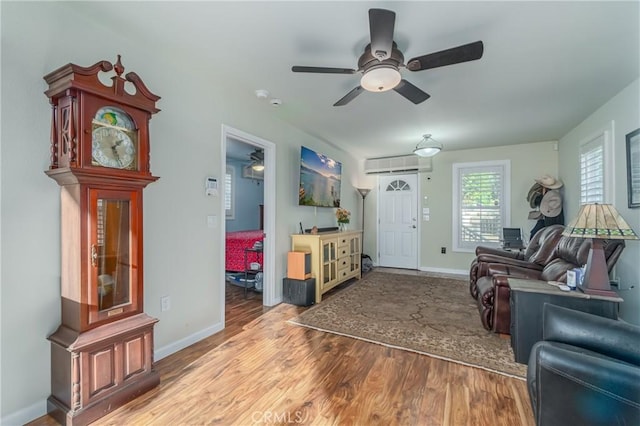 living room with an AC wall unit, ceiling fan, baseboards, and wood finished floors