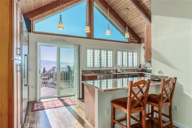 kitchen with a peninsula, wood finished floors, wood ceiling, light stone countertops, and beamed ceiling