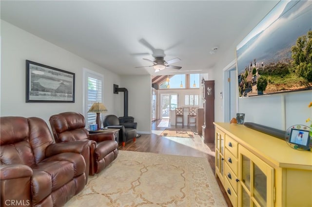 living area with wood finished floors, a wood stove, and a ceiling fan