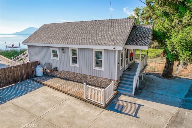 view of front of home featuring a water view, fence, a patio, and roof with shingles