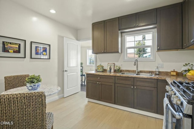 kitchen featuring stainless steel gas stove, light wood-style flooring, a sink, baseboards, and dark brown cabinets