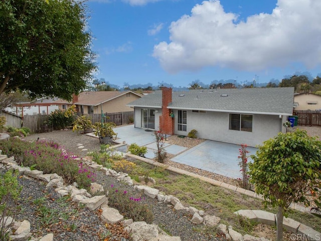 rear view of property featuring stucco siding, a fenced backyard, a shingled roof, and a patio