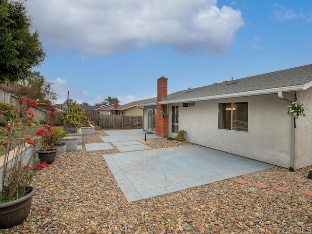 back of property featuring a patio, a fenced backyard, a shingled roof, stucco siding, and a chimney