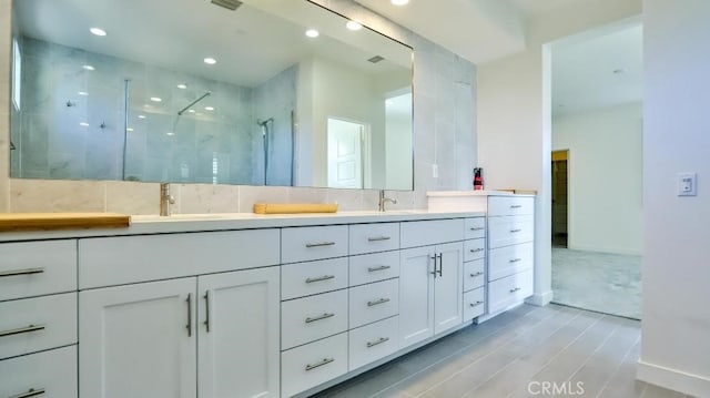 full bathroom with double vanity, a tile shower, a sink, and recessed lighting