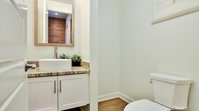 half bathroom with toilet, baseboards, wood finished floors, and vanity