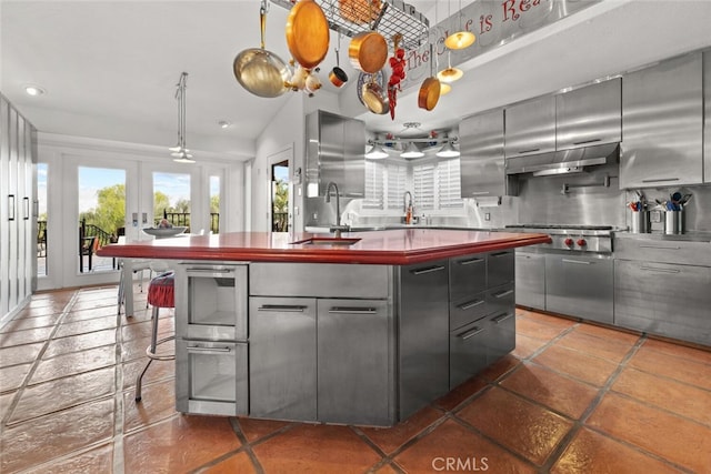 kitchen featuring a center island with sink, stainless steel gas cooktop, gray cabinets, a sink, and under cabinet range hood