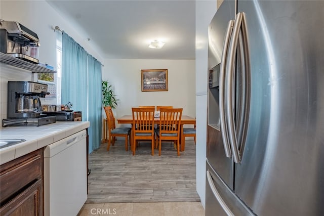 kitchen with light wood-type flooring, open shelves, tile countertops, stainless steel fridge, and white dishwasher