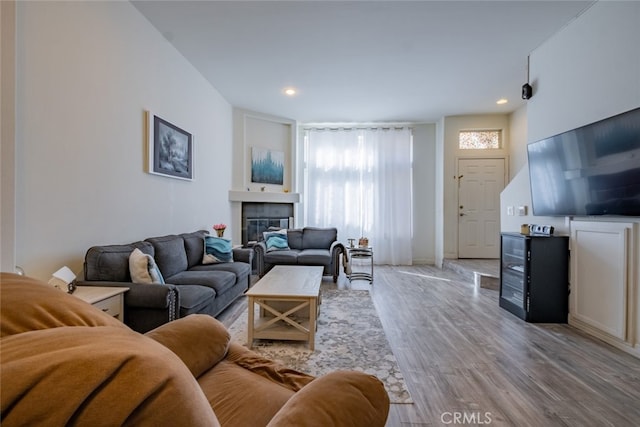 living area with recessed lighting, light wood-style floors, and a glass covered fireplace