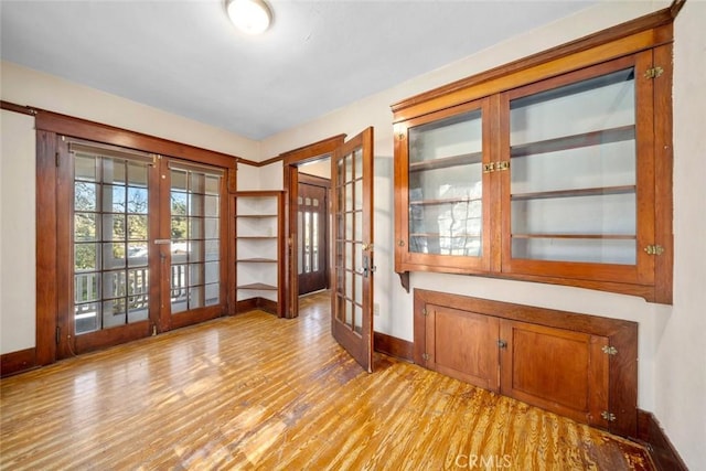 empty room featuring light wood-type flooring, french doors, and baseboards