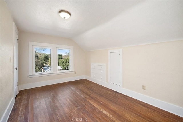 additional living space featuring vaulted ceiling, dark wood-style floors, and baseboards