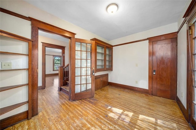 spare room featuring french doors, baseboards, light wood-style floors, and stairs