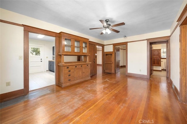 unfurnished living room with light wood finished floors, baseboards, and ceiling fan