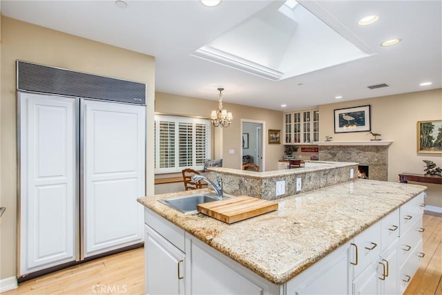 kitchen with light wood finished floors, a high end fireplace, light stone counters, a sink, and recessed lighting