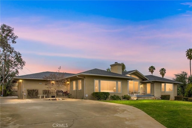 view of front of property featuring driveway, a chimney, a front lawn, and stucco siding