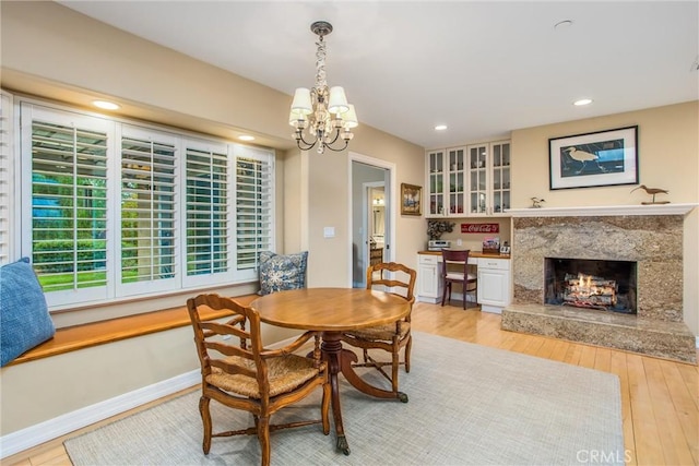 dining room featuring baseboards, light wood-style flooring, a premium fireplace, built in desk, and recessed lighting