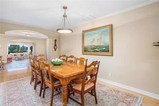 dining space featuring arched walkways, light wood-style flooring, visible vents, baseboards, and ornamental molding