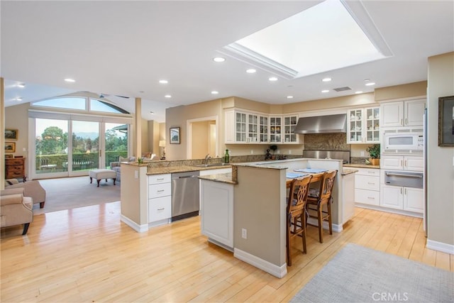 kitchen with a warming drawer, stainless steel dishwasher, white microwave, open floor plan, and wall chimney range hood