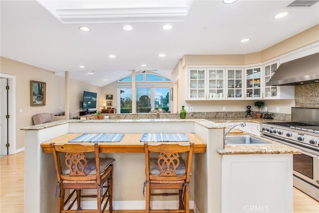 kitchen featuring light wood-style flooring, gas stove, open floor plan, a sink, and light stone countertops