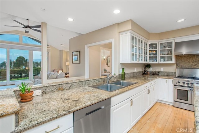 kitchen with light wood-style flooring, appliances with stainless steel finishes, light stone countertops, wall chimney range hood, and a sink