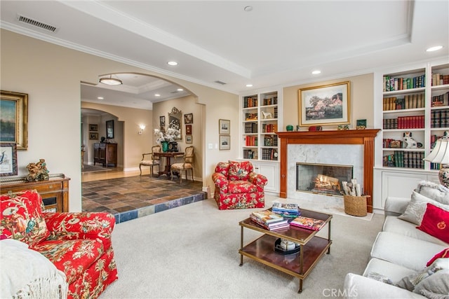 carpeted living area with visible vents, arched walkways, a raised ceiling, built in features, and recessed lighting