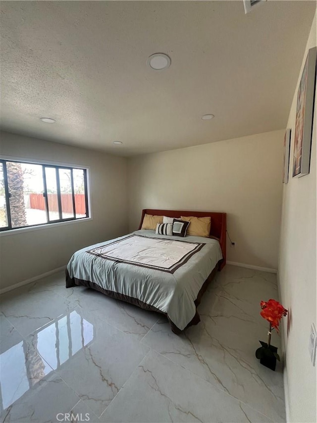 bedroom featuring marble finish floor, a textured ceiling, and baseboards