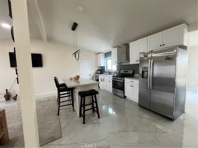 kitchen with marble finish floor, stainless steel appliances, white cabinetry, a sink, and wall chimney range hood