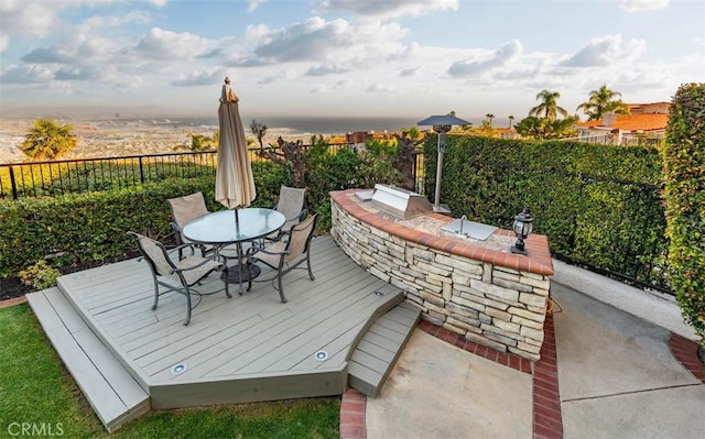 wooden deck with grilling area, outdoor dining area, an outdoor kitchen, and a fenced backyard