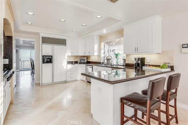 kitchen featuring a peninsula, a breakfast bar, paneled built in fridge, dishwasher, and a tray ceiling