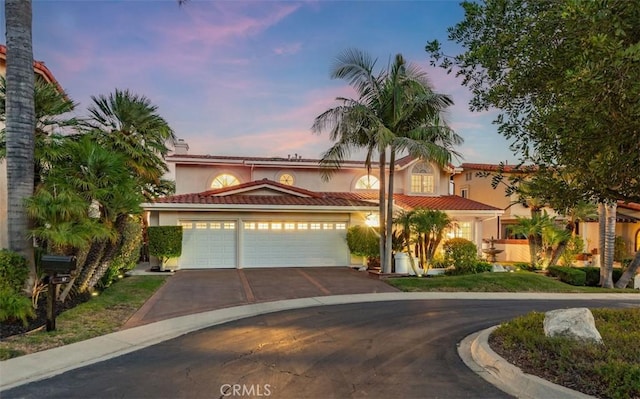 mediterranean / spanish house featuring a garage, a tile roof, aphalt driveway, and stucco siding