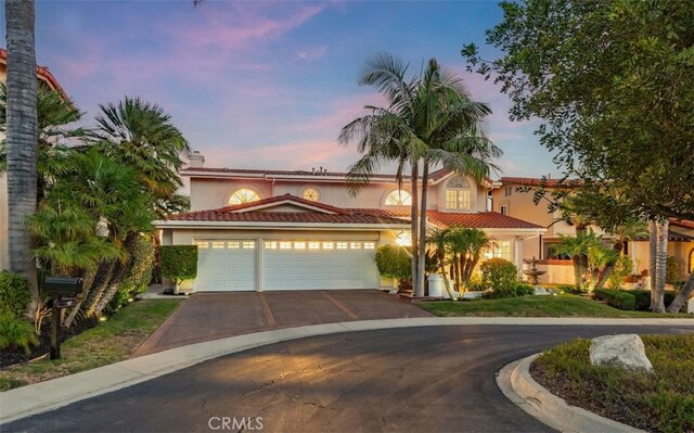 mediterranean / spanish home with an attached garage, stucco siding, a tiled roof, and concrete driveway