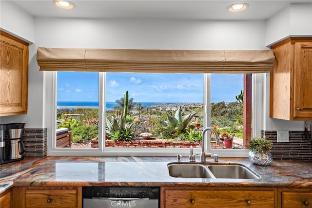 kitchen with dark stone counters, decorative backsplash, brown cabinets, stainless steel dishwasher, and a sink