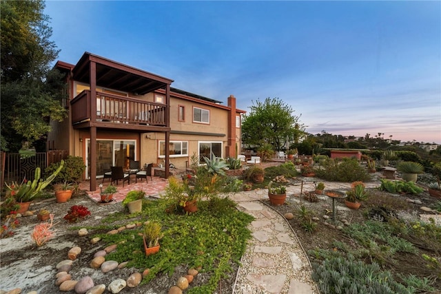 rear view of property with a balcony, fence, a chimney, stucco siding, and a patio area