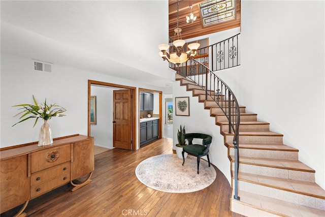 staircase featuring a notable chandelier, a towering ceiling, visible vents, and hardwood / wood-style floors