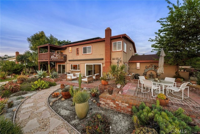 back of property featuring a patio, a wooden deck, a chimney, stucco siding, and an outdoor hangout area