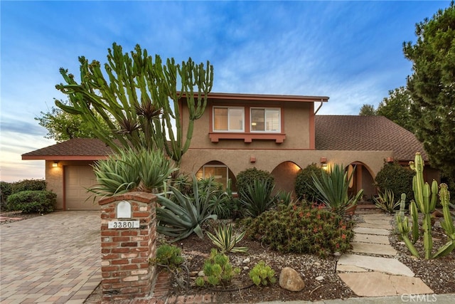 view of front of property featuring decorative driveway, an attached garage, and stucco siding