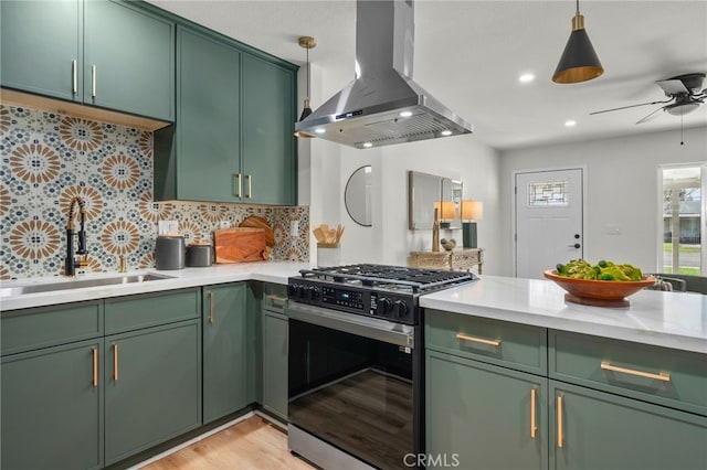 kitchen with a sink, wall chimney range hood, green cabinets, and gas range oven