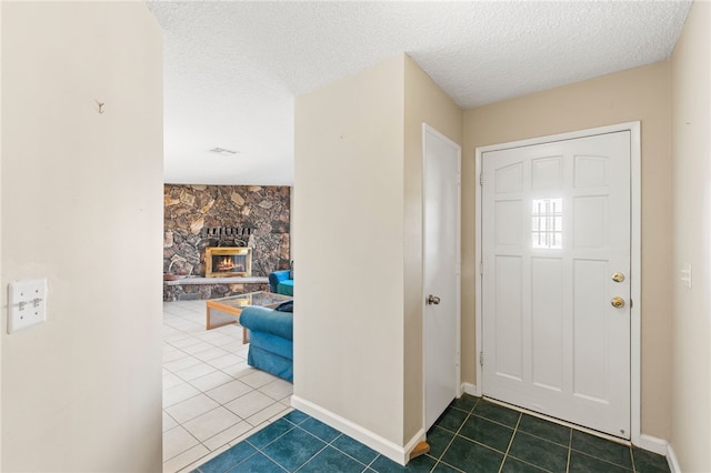 tiled foyer entrance with a textured ceiling, a stone fireplace, and baseboards