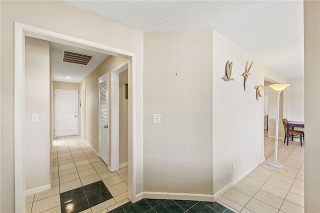 hallway featuring baseboards, visible vents, a textured ceiling, and tile patterned floors