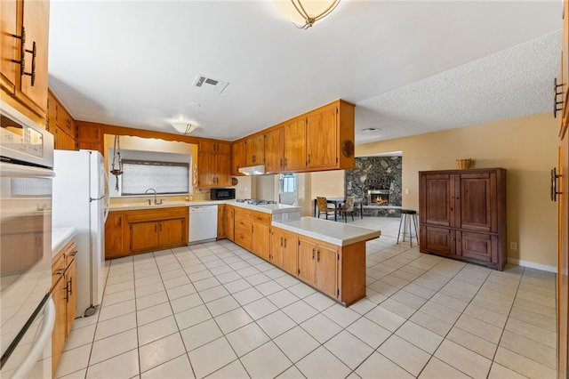 kitchen with white appliances, visible vents, a peninsula, light countertops, and light tile patterned flooring