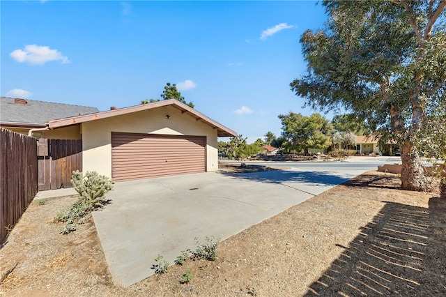 view of property exterior with an attached garage, fence, concrete driveway, and stucco siding