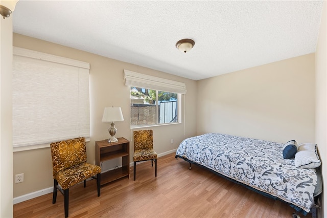 bedroom with a textured ceiling, wood finished floors, and baseboards