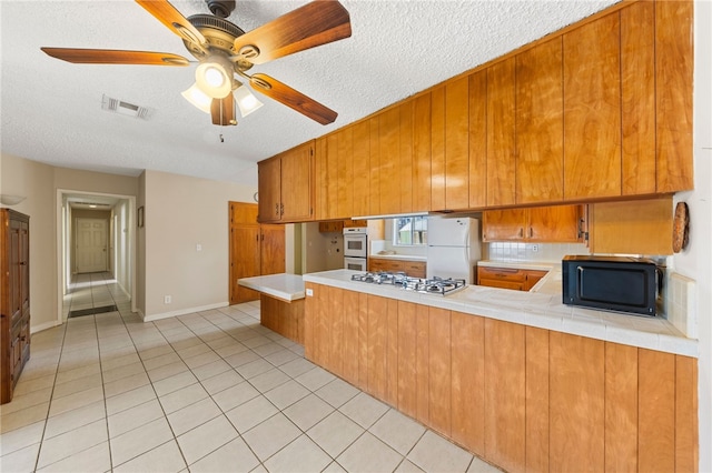 kitchen with brown cabinets, white appliances, visible vents, and a peninsula