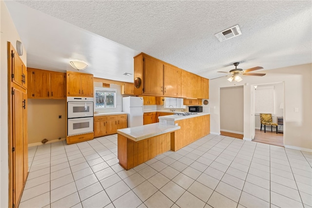 kitchen with white appliances, visible vents, a peninsula, light countertops, and light tile patterned flooring