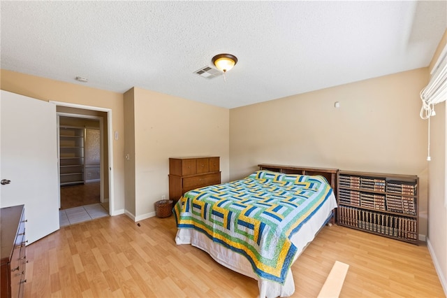 bedroom with a textured ceiling, wood finished floors, visible vents, and baseboards