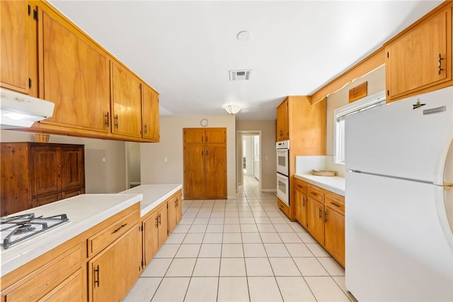 kitchen featuring light tile patterned floors, light countertops, visible vents, white appliances, and under cabinet range hood