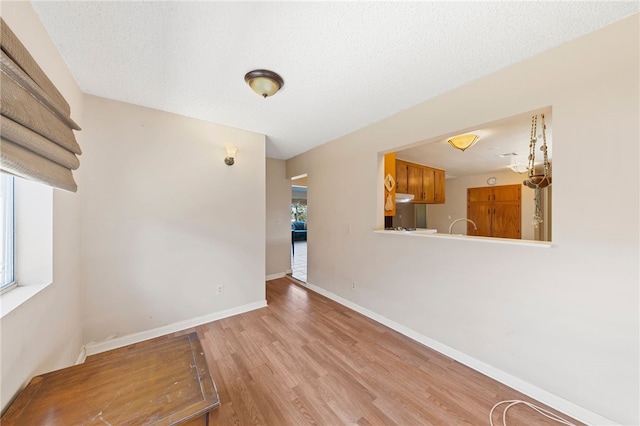 empty room featuring a wealth of natural light, a textured ceiling, baseboards, and wood finished floors